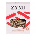 Image shows a compact rectangular packet of Zymi Organic Bites with carob, dotted with black and white sesame seeds. The wrapper uses warm brown and cream tones, displaying a close-up of the seed-speckled bites, a simple logo and minimal natural imagery on a neutral background. Soft lighting reveals