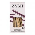 A bundle of slender, golden-brown breadsticks lies on a wooden board, each stick studded with dark Kalamata olive pieces and scattered thyme and oregano leaves. Cracked crusts reveal an airy, rustic interior; loose olives and herb sprigs frame the scene.