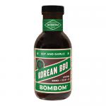 A front-facing photo shows six Bombom Korean BBQ Soy & Garlic tubs arranged in neat rows on a shelf. Rich brown sauce is visible through clear lids, labels feature Hangul and English text, garlic and soy illustrations, glossy packaging reflecting bright studio lighting Subtle droplets dot some lids