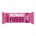 A neat rectangular bar of pale cream fudge rests on a neutral surface, scored into thick segments. Its glossy top shows tiny Madagascan vanilla specks. A partially peeled simple wrapper reveals soft, slightly sticky edges and gentle shadows that define texture and form. Bright highlights catch sheen