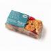 A single Paradise flapjack sits on a tray amid eleven identical bars, each rectangular and golden-brown with visible oats and a glossy syrup glaze. Clear wrapper displays bright bakery branding and a product label, while the tray forms tidy rows under soft lighting.