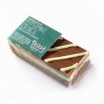 A rectangular tray holds 12 square peppermint-crunch traybakes arranged in neat rows. Each bar has a dark chocolate base, pale mint filling and glossy white icing scattered with crushed red-and-white peppermint and delicate green drizzle, the surface catching soft studio light. Subtle crumbs dot edges.