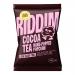 Glossy brown and cream snack bags display the Riddim Snacks logo and Cocoa Tea label over stylized popcorn and a steaming teacup illustration. Multiple single-serve packets arrange in a neat grid, their shiny wrappers reflecting studio light and emphasizing warm cocoa tones. Soft sheen catches light