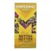 A neatly wrapped Montezuma's Butter Nutter chocolate bar sits against a neutral background. The glossy wrapper shows the Montezuma's logo and a stylized peanut motif. A broken piece reveals smooth, caramel-colored peanut butter filling and glossy milk chocolate studded with nut pieces.