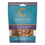 A glossy Cambrook Hickory Smoke seasoned giant corn bag sits upright. Amber roasted kernels show through a clear window, dusted with smoky spice. Orange and brown packaging displays the Cambrook logo and product name with subtle nut illustrations.