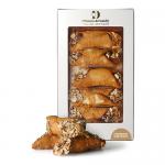 A rustic box of six cannoli sits on a wooden surface, each tube filled with creamy hazelnut filling and dusted with cocoa and chopped toasted hazelnuts. Packaging shows Di Santo & Family Bakery branding with warm, artisanal typography and a simple, vintage label. Linen napkin peeks out from beneath.