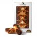 A photo shows six tiramisù cannoli in a clear tray. Each golden-brown shell holds a smooth coffee-mascarpone cream piped from both ends and dusted with cocoa. The carton displays Di Santo & Family Bakery branding and a small window reveals the pastries. Soft light highlights a soft sheen on filling.