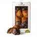 A close-up photograph shows four round Rocher chocolates arranged in a neat row inside a partially open Di Santo & Family Bakery box. Each confection displays a glossy chocolate coating studded with chopped hazelnut pieces, set against a simple cream insert and rustic branded packaging. in soft glow