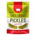 The photo shows small green pickles speckled with red chilli flakes and seeds, glistening with brine. They sit beside branded Serious Pig Charcuterie packaging featuring a pig logo and bold text. Lighting highlights the pickles' texture and sheen against a neutral background.