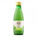 A clear glass bottle of Biona Organic lime juice stands upright with a bright green label and images of sliced limes. The pale green liquid glows inside. Scattered around the bottle lie small piles of grains and dried ingredients on a white background, with soft studio lighting. Subtle studio sheen