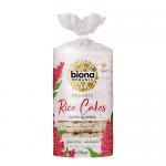 Bright cardboard box features green and white branding with a clear product name and nutritional icons. Inside, twelve round, pale-brown puffed rice cakes studded with tiny quinoa grains sit in a neat stack, visible through a transparent wrap that shows texture and grain flecks. A natural kraft look.