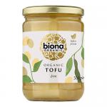White rectangular tubs of Biona Organic Plain Tofu sit in a flat six-pack arrangement. Green Biona logo and simple typographic labels appear on each pack, paired with a pale green and cream color scheme. Moist, pale cream tofu blocks are visible through translucent lids. Sealed lids glint under studio