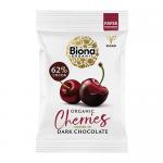 A compact rectangular box displays Biona Organic Dark Chocolate Cherries branding in deep brown and red tones. Glossy cherries and dark chocolate pieces appear front-center. Natural ingredient icons and a clear weight label sit beside simple botanical illustrations. Matte paper texture, subtle seal.