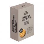 Close-up image shows a pale box of Drinks Bakery 'Gruyère Cheese & Tarragon' biscuits beside loose golden rounds. Crackers show cheese flecks and tiny herb pieces; fresh tarragon sprigs and a crumpled linen napkin sit on a weathered wooden board under soft, natural light.