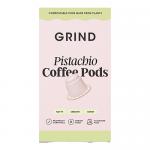 An image shows a compact box of Grind Coffee Roasters Pistachio Blend pods. Matte pistachio-green and kraft-brown packaging displays pistachio illustrations, a home-compostable icon and a 90g weight mark. An open flap reveals neatly arranged foil-sealed pods beside a small stack. Soft natural light.