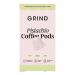 An image shows a compact box of Grind Coffee Roasters Pistachio Blend pods. Matte pistachio-green and kraft-brown packaging displays pistachio illustrations, a home-compostable icon and a 90g weight mark. An open flap reveals neatly arranged foil-sealed pods beside a small stack. Soft natural light.