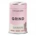 A compact matte tin of Grind Coffee Instant House sits on a neutral surface. Its 90g cylindrical container features a minimalist black label with white logo and bronze accent, a screw-top lid, small descriptive text and a stylized coffee-bean graphic beside clean typography. Matte sheen shows detail