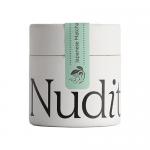 A set of six matte green tins labeled 'Nuditea' lines a shelf against a soft beige background. One tin opens to reveal finely ground, vivid emerald matcha. Simple Japanese characters and a small white 30g mark appear on the minimalist labels; a wooden scoop and a dusting of powder sit nearby always.