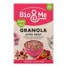 A tall matte box with vivid berry illustrations and a clear window reveals clusters of granola studded with dried berries and seeds. The bold logo sits above nutritional text and pastel accents; a torn-open corner shows crunchy oat clusters spilling onto a white surface. Soft shadows fall across it.