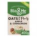 A bright cardboard pack shows the Bio&Me logo at top, vivid red apple slices and cinnamon sticks beside a steaming bowl of porridge with visible oats. Green accents, subtle grain textures and clean white background create a fresh, natural visual presentation. Soft shadows fall and small icons appear