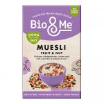 A resealable 450g Bio&Me Fruit & Nut muesli bag stands upright with a cream-and-green label and fruit illustrations. Loose muesli spills onto a wooden surface, revealing oats, dried cranberries, raisins, almonds and hazelnuts; a wooden scoop rests nearby.