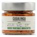Glass jar displays chunky mixed-vegetable bruschetta in glossy olive oil. Diced red tomatoes, green peppers, onions and herbs form a colorful, textured mix. A simple label reads Casalinga with rustic typography; metal lid reflects light and seals the jar. Oil sheen highlights herb flecks across lid.