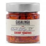 Bright ruby-hued semi-dried cherry tomatoes glisten in oil inside a clear glass jar. Wrinkled skins and soft, tender flesh form textured clusters; a few basil leaves and crushed peppercorns float among glossy tomatoes. A rustic label wraps the jar, hinting at homemade style. Soft oil sheen, catching
