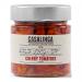 Bright ruby-hued semi-dried cherry tomatoes glisten in oil inside a clear glass jar. Wrinkled skins and soft, tender flesh form textured clusters; a few basil leaves and crushed peppercorns float among glossy tomatoes. A rustic label wraps the jar, hinting at homemade style. Soft oil sheen, catching