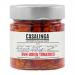 Glass jar holds chargrilled sundried tomatoes packed in golden oil. Deep crimson tomato halves show charred edges and wrinkled texture; flecks of herbs and sliced garlic float among glossy pieces. The jar carries a rustic label with the Casalinga name and simple graphic Soft oil sheen catches light