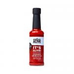 The photo shows a 150ml glass bottle of Eaten Alive Smoked Sriracha fermented hot sauce. Deep russet-red sauce swirls inside. A rustic cream label features bold black lettering, chilli and smoke graphics. Metal cap glints; bottle rests on a weathered wooden surface against a dark backdrop. dimly lit.