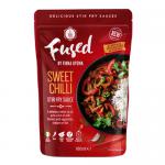 Bright red-orange sweet chilli stir-fry sauce fills a clear jar, its glossy, syrupy surface studded with chilli flakes and seeds. The label reads Fused by Fiona Uyema Dressings & Sauces in simple, modern type. Soft side lighting emphasizes texture and vibrant color.