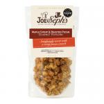 A kraft-style pouch displays the Joe & Seph’s logo above a clear window revealing glossy amber-coated popcorn studded with toasted pecan halves. Maple syrup glaze catches light, forming a sticky sheen; scattered pecans and caramelized kernels create a warm, rustic composition With warm nutty flecks