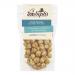 A glossy pouch of Joe & Seph’s Salted Caramel Popcorn sits upright, showing warm golden caramel kernels through a clear window. The brand logo and whimsical illustrations frame the bag; scattered popped corn and salt crystals outline the shiny, sticky coating. Muted kitchen tiles form a soft backdrop
