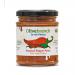 Glass jar of Olive Branch Mezze Red Pepper Paste sits on a pale surface. The label displays an olive branch logo, contrasting red and green panels and bold type. Vivid red paste shows through the glass, its surface slightly textured beneath a silver metal lid. A narrow white sticker circles the jar.