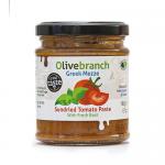 Glass jar labeled Olive Branch Mezze holds dense, deep-red sun-dried tomato paste. Sunlit, glossy surface shows rich texture. Rustic label with olive-branch motif sits against a wooden board, surrounded by dried tomatoes, a sprig of oregano and a drizzle of olive oil. Soft shadows pool near the jar.