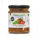 Glass jar labeled Olive Branch Mezze holds dense, deep-red sun-dried tomato paste. Sunlit, glossy surface shows rich texture. Rustic label with olive-branch motif sits against a wooden board, surrounded by dried tomatoes, a sprig of oregano and a drizzle of olive oil. Soft shadows pool near the jar.