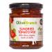 A glass jar displays a colorful mezze blend of green and black olives, chunks of sun-dried tomato, slivers of garlic and herb flecks suspended in glossy olive oil. A rustic label wraps the jar, while light highlights the briny textures and rich, red tomato pieces. Warm light frames the jar rims now.