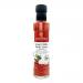 Six clear cylindrical bottles show ruby-red sweet chilli and garlic sauce with flecks of chilli and garlic. Each bottle bears a white label with The Coconut Kitchen logo, coconut illustration and product name. Silver screw caps gleam under bright studio lighting on a white background. Tidy alignment