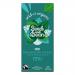 A wrapped Seed & Bean extra-dark chocolate bar sits on a neutral background. The packaging displays 72% extra dark and mint with small mint-leaf artwork and illustrations of seeds. A torn corner reveals a dark, glossy chocolate slab flecked with tiny seeds. A thin silver foil peeks from the wrapper.
