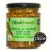 A glass jar of olive tapenade shows a coarse, dark-green spread topped with crumbled white goat’s cheese, a few fresh rosemary sprigs and thin red chilli slices. The jar rests on a rustic wooden board beside scattered olives and coarse sea salt. Warm light highlights glossy olive sheen.