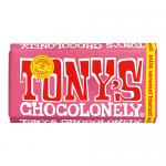 A brightly colored wrapper shows bold yellow and red blocks with an oversized handwritten logo. A milk chocolate bar with irregular, chunky segments sits partly unwrapped, revealing caramel and crunchy biscuit pieces. A Fairtrade emblem appears on the lower corner. The metal glints at the torn edges.