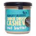 Six glass jars of Hungry Squirrel Cookie Dough Cashew 180g sit clustered on a wooden surface. Creamy tan spread peeks through labels adorned with cashew illustrations and cookie dough imagery. Metal lids catch light; crumbs and a wooden spoon add rustic texture against a neutral backdrop. soft hues.