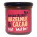 Photo shows six 180 g jars of Hungry Squirrel Hazelnut & Cacao spread arranged in two rows of three on a neutral surface. Clear glass jars reveal glossy brown spread; labels feature a stylized squirrel, product name and icons; silver lids reflect light. soft shadows and subtle reflections add depth.