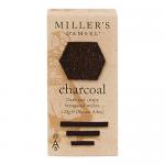 A photo shows round charcoal wafers with matte black-gray surfaces and delicate crumbly edges. A simple kraft sleeve with a minimalist bakery label and clear window reveals six biscuits. Soft side light emphasizes texture, crumbs, and a faint dusting of flour.