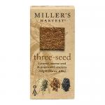 A slim rectangular packet rests on a wooden surface; six thin, round wafers peek through a clear window. Each wafer displays golden-brown crisp edges and a scattering of sunflower, flax and sesame seeds. Natural kraft tones and simple branding frame the scene. A subtle matte finish softens the light.