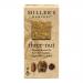 Image shows a neatly arranged stack of thin golden-brown wafers with visible hazelnut, almond and walnut pieces, beside a rustic kraft-paper packet labeled Miller’s Harvest. Soft natural light highlights the crunchy texture and scattered nut fragments on a wooden surface.