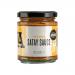 A glossy glass jar shows creamy peanut satay sauce in a warm tan color. The label features bold red and white lettering that reads J & A Food, with a small peanut illustration and Janda Chutney & Condiments branding. A silver metal lid caps the jar against a neutral background. Soft studio lighting.