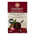 Two small clear jars of vivid red curry paste sit side by side, the glossy scarlet paste visible through glass. Clean white labels display a bold brand name and coconut motif. A cardboard carrier holds six identical twin-packs, arranged neatly on a neutral background. Lighting highlights the paste.
