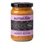 Six 285g jars of Butter Bike Co Almost Smooth peanut butter sit in a neat cluster, amber contents visible through clear glass. Creamy-spread labels feature a bicycle logo and bold type. Light reflects off metal lids and smooth surfaces, casting soft shadows.