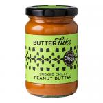 A pack of six 285g Butter Bike Co Smoked Chilli Peanut Butter jars stands in a neat row. Clear glass reveals rich reddish-brown spread; cream labels display the brand logo and chilli illustration, while dark lids catch studio light against a plain backdrop.